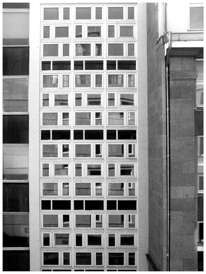The outside of a prefab staircase. A grid-like pattern contains windows and concrete layers for the floots. The pattern looks like morse code.