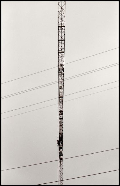 A construction crane as seen from below. The perspective creates the illusion of a straight line, vertical in the frame. Some power lines cut it diagonally.